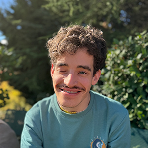 Antón, joven adulto con cabello rizado oscuro, bigote incipiente y expresión amable