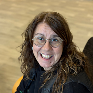 Marta, mujer adulta con cabello largo castaño claro, gafas de ver redondas y una sonrisa con enfásis