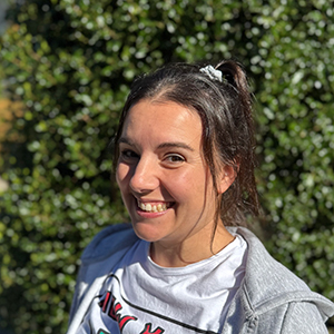 Sandra, mujer joven con cabello largo castaño oscuro recogido, expresión amistosa con gran sonrisa